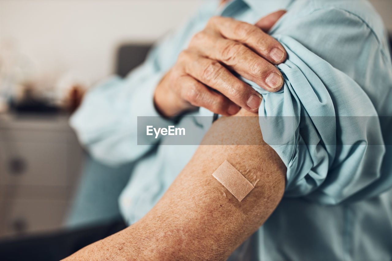 Senior man patient holding shirt sleeve up with a plaster in place of injection of vaccine