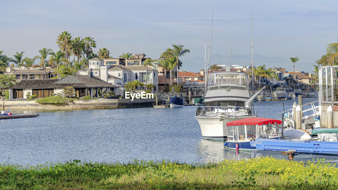 SAILBOATS MOORED AT HARBOR BY RIVER AGAINST BUILDINGS