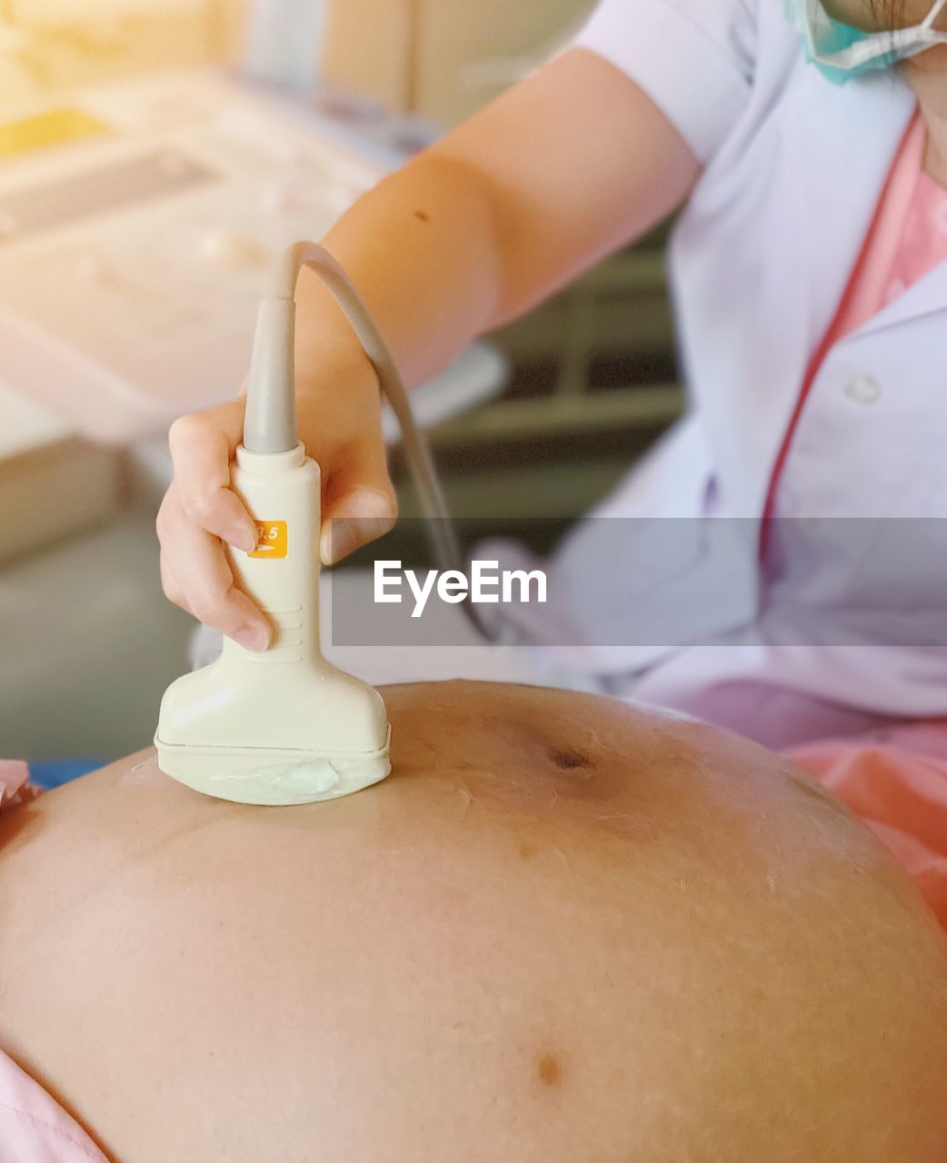 Midsection of technician performing ultra sound on pregnant woman