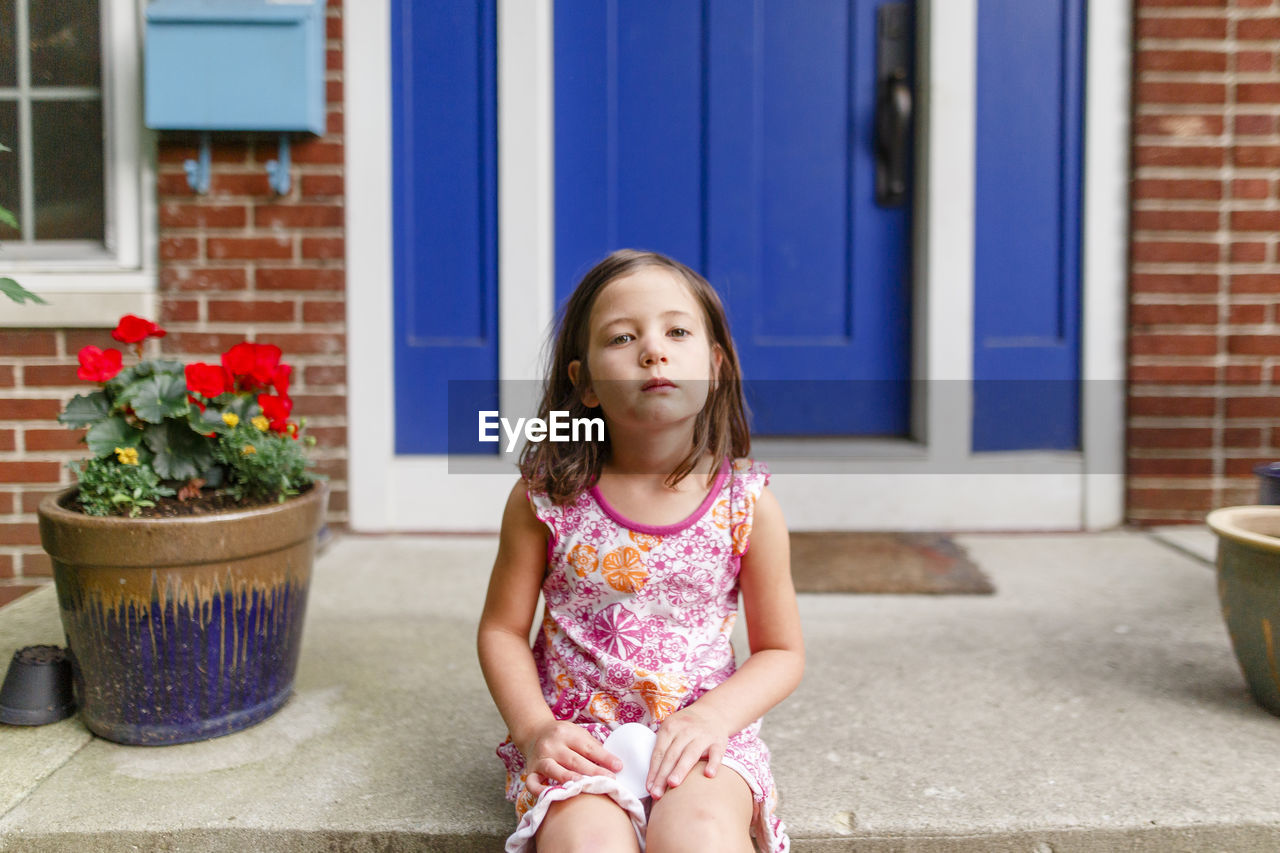 A small child sits on front stoop of her home with serious expression