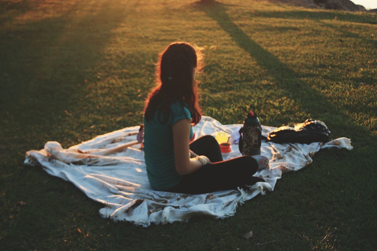 Side view of woman sitting on picnic blanket at park