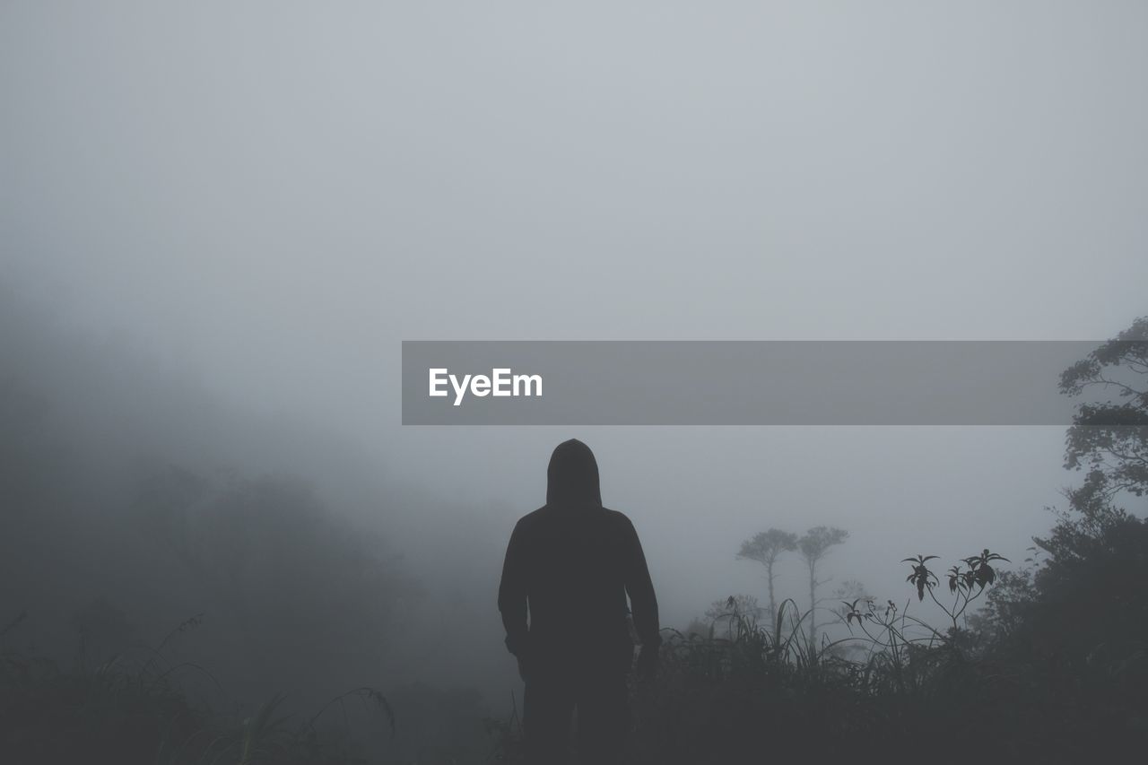 Rear view of silhouette man standing on landscape in foggy weather