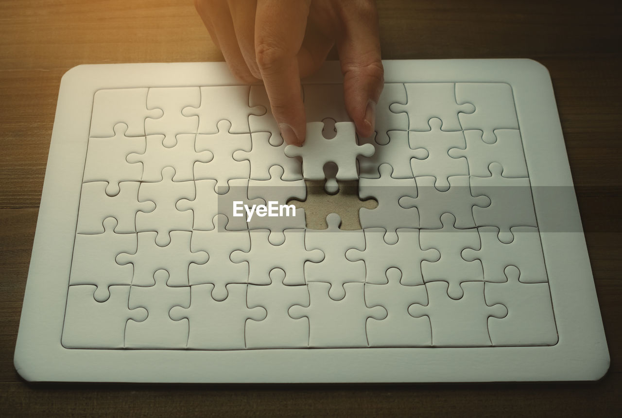 High angle view of person hand holding jigsaw piece by puzzle on table