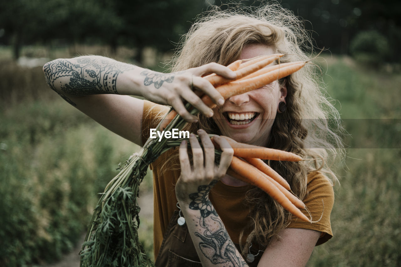 Female farmer smiling while holding carrots at farm