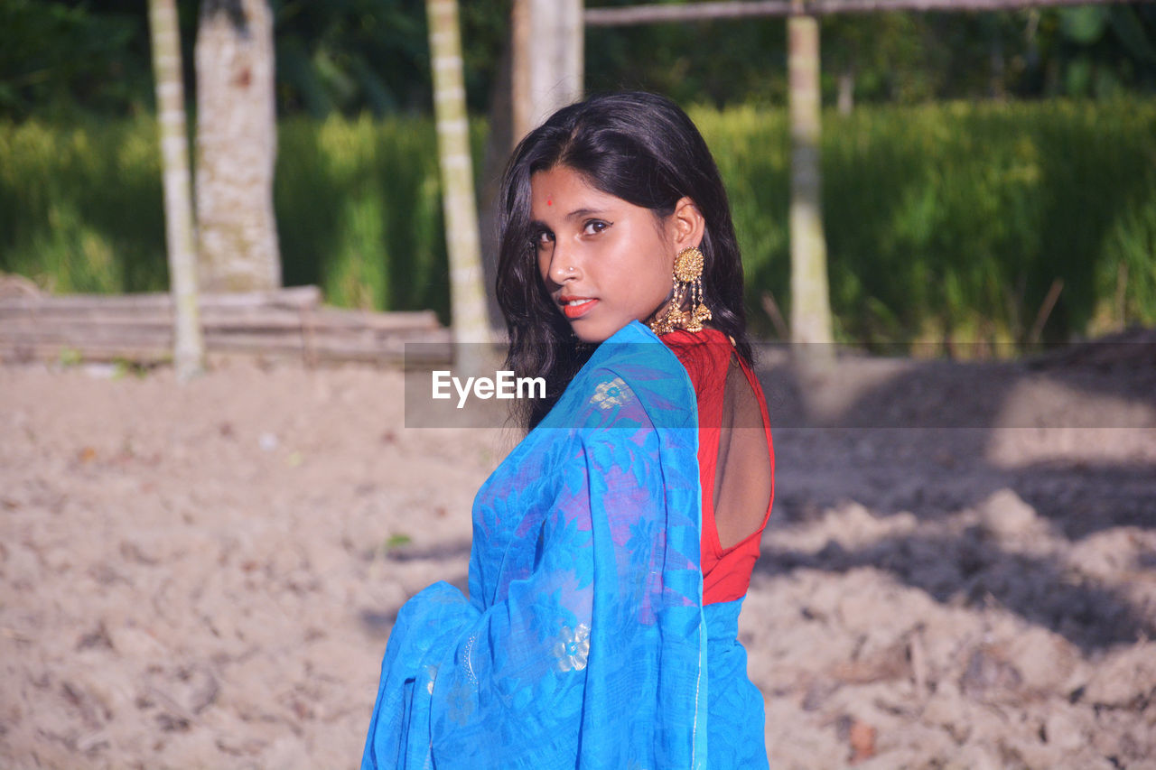 PORTRAIT OF BEAUTIFUL YOUNG WOMAN STANDING ON LAND