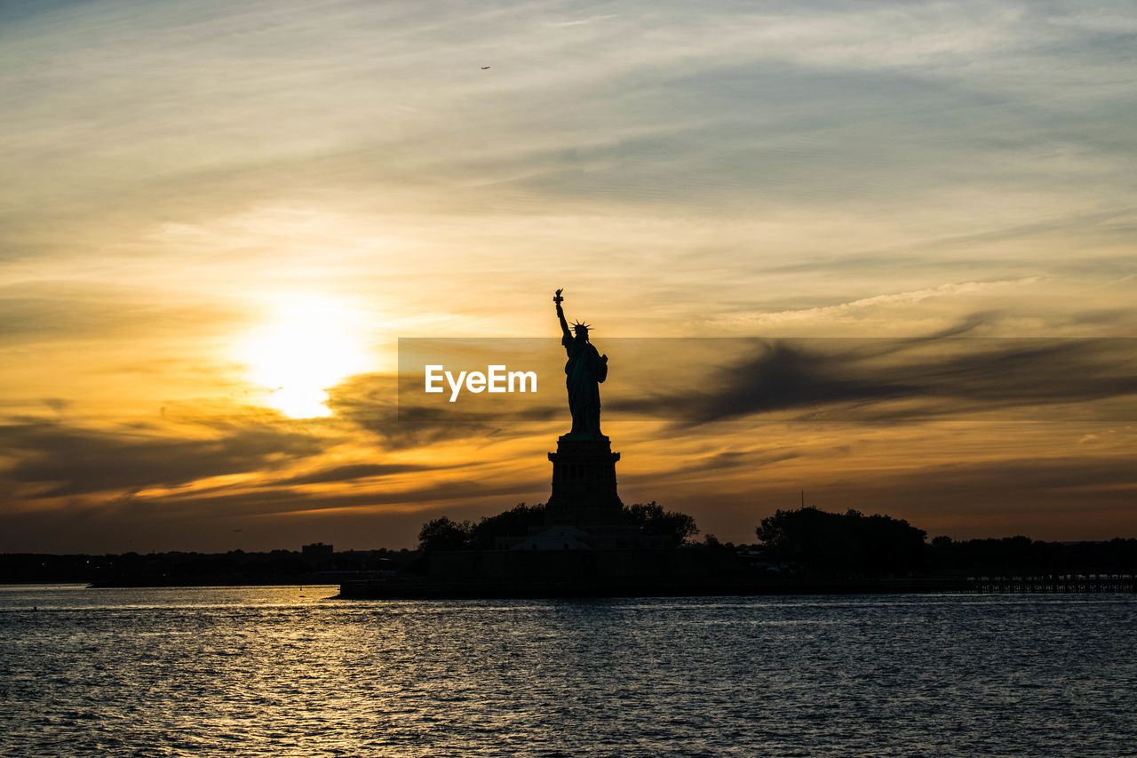 Silhouette statue of liberty against cloudy sky during sunset