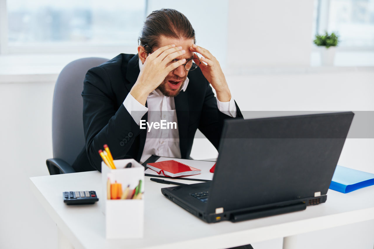 YOUNG WOMAN USING SMART PHONE WHILE SITTING IN OFFICE