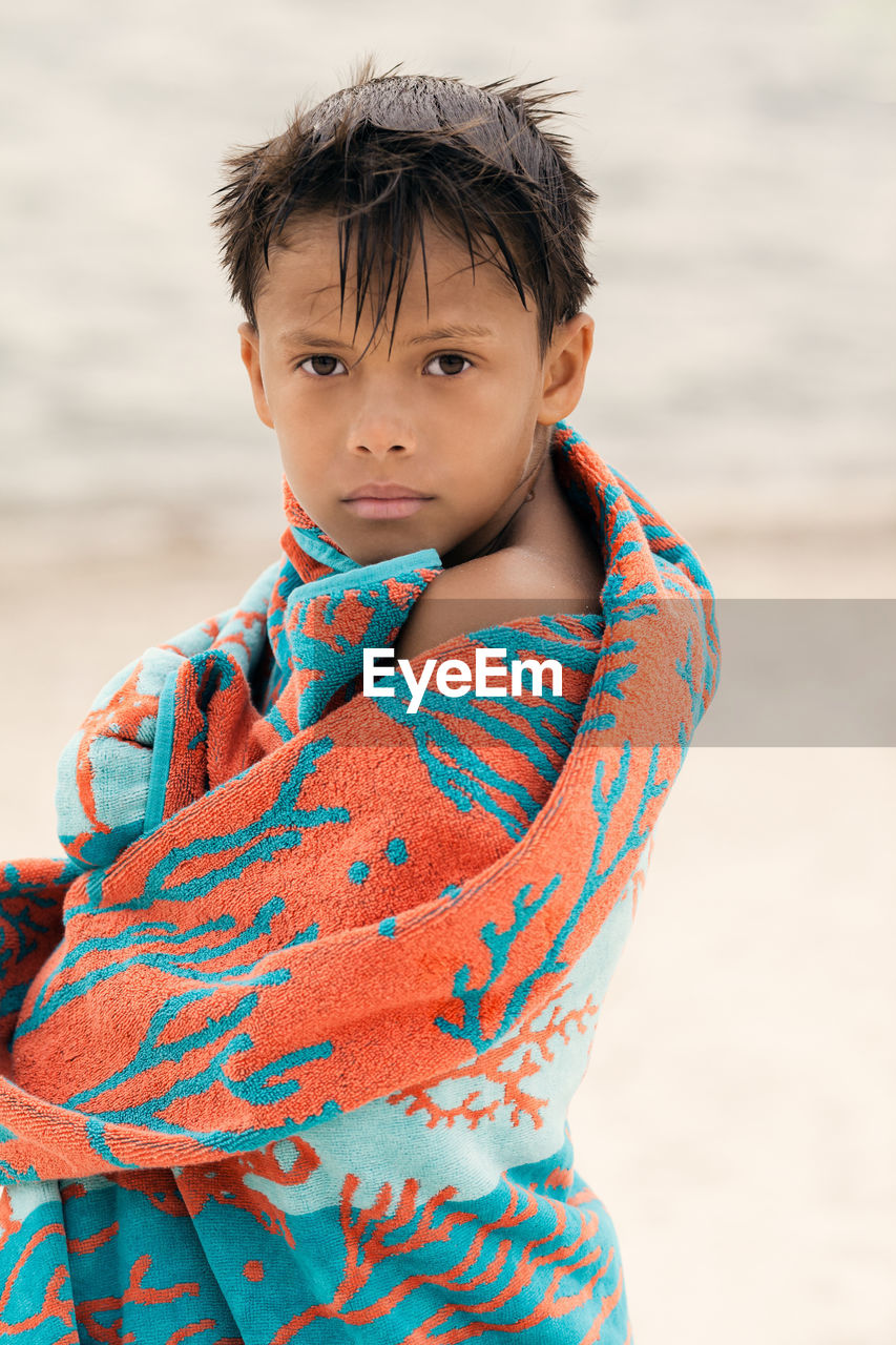 Little boy wrapped in a beach towel standing near river and looking at camera, summer portrait 