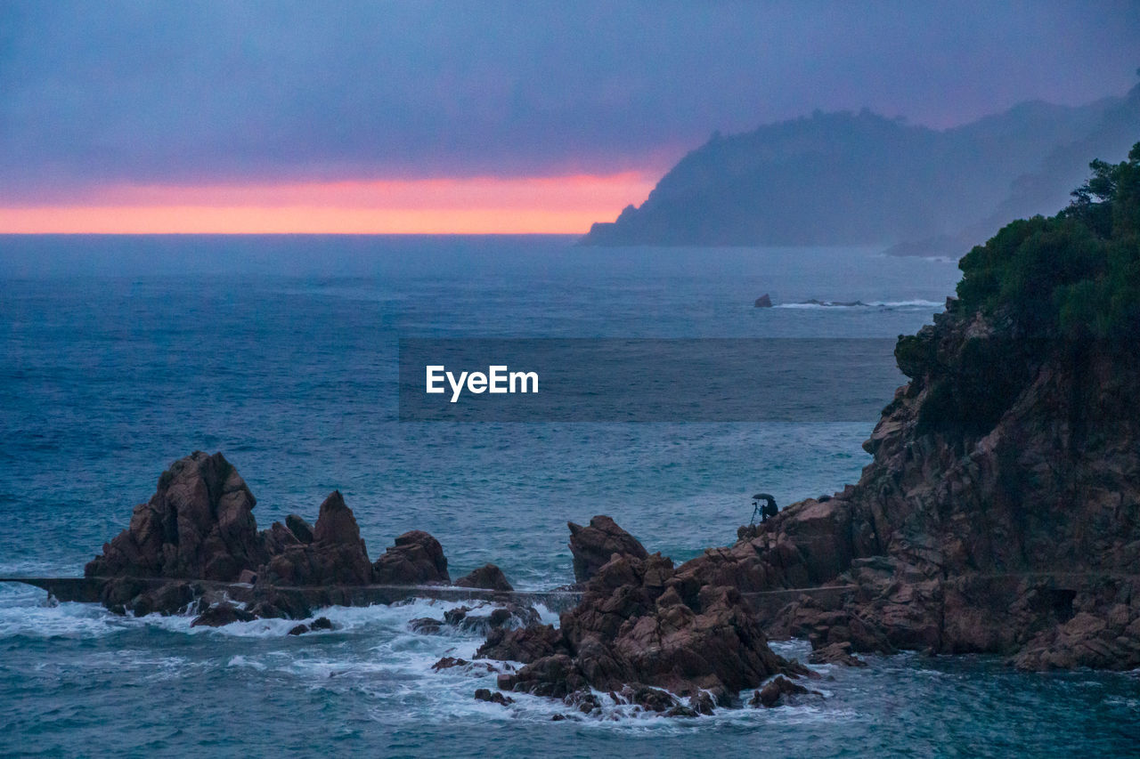 Scenic view of sea against sky during sunset.  the time is raining. and man shot a photo of the sea
