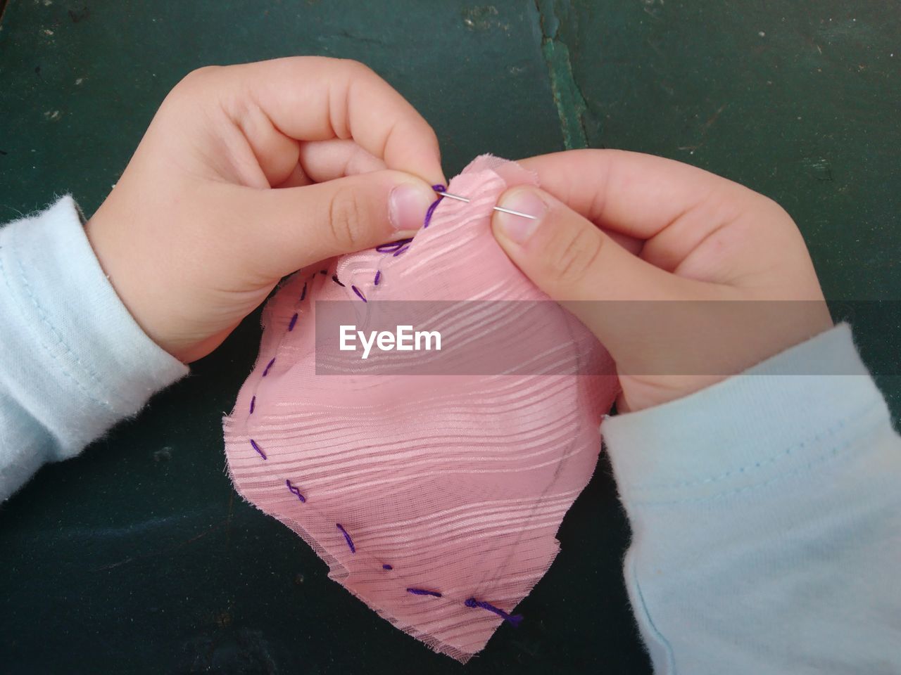 Cropped hands of child stitching fabric on table