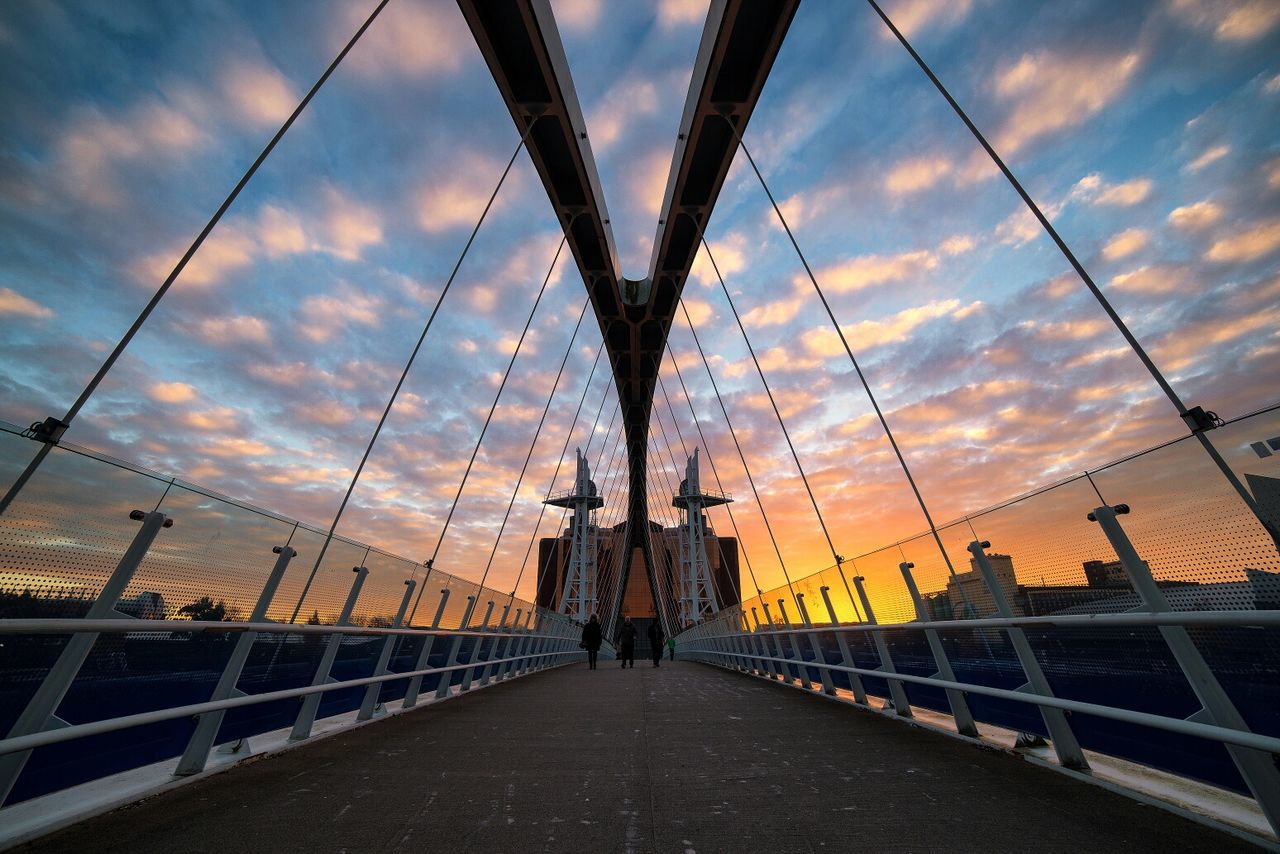 Lowry footbridge against cloudy sky at sunset