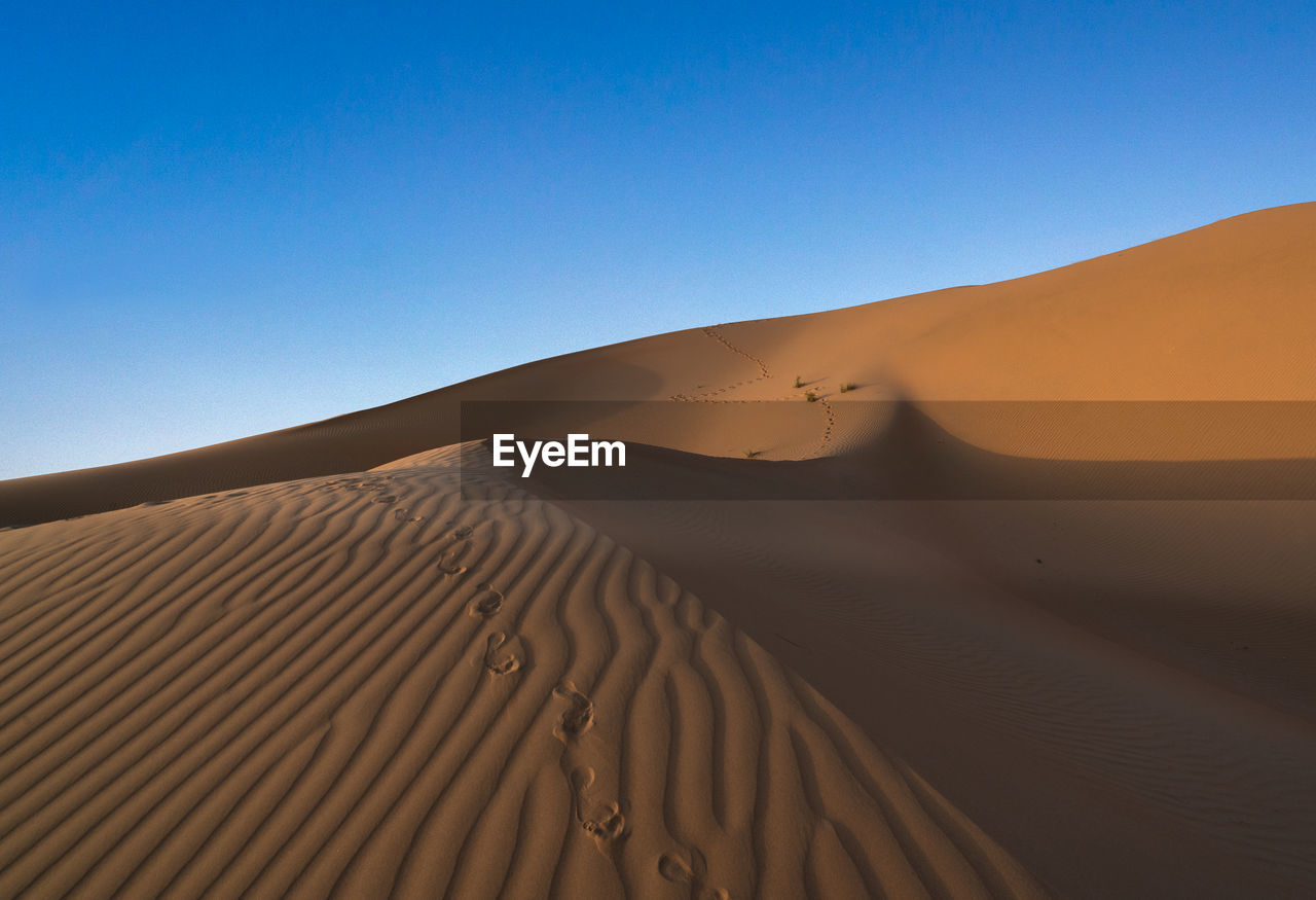 Low angle view of sand dunes against clear blue sky