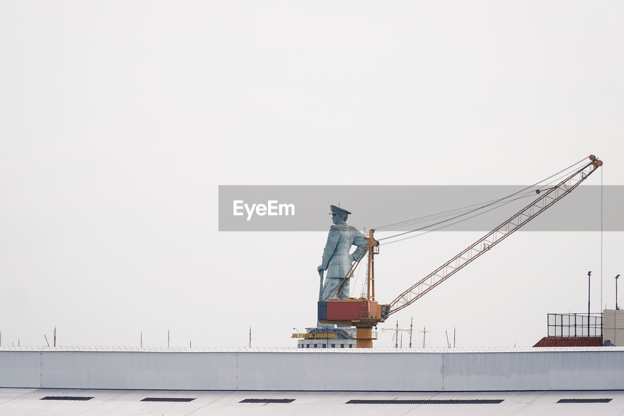 Low angle view of crane by building against clear sky