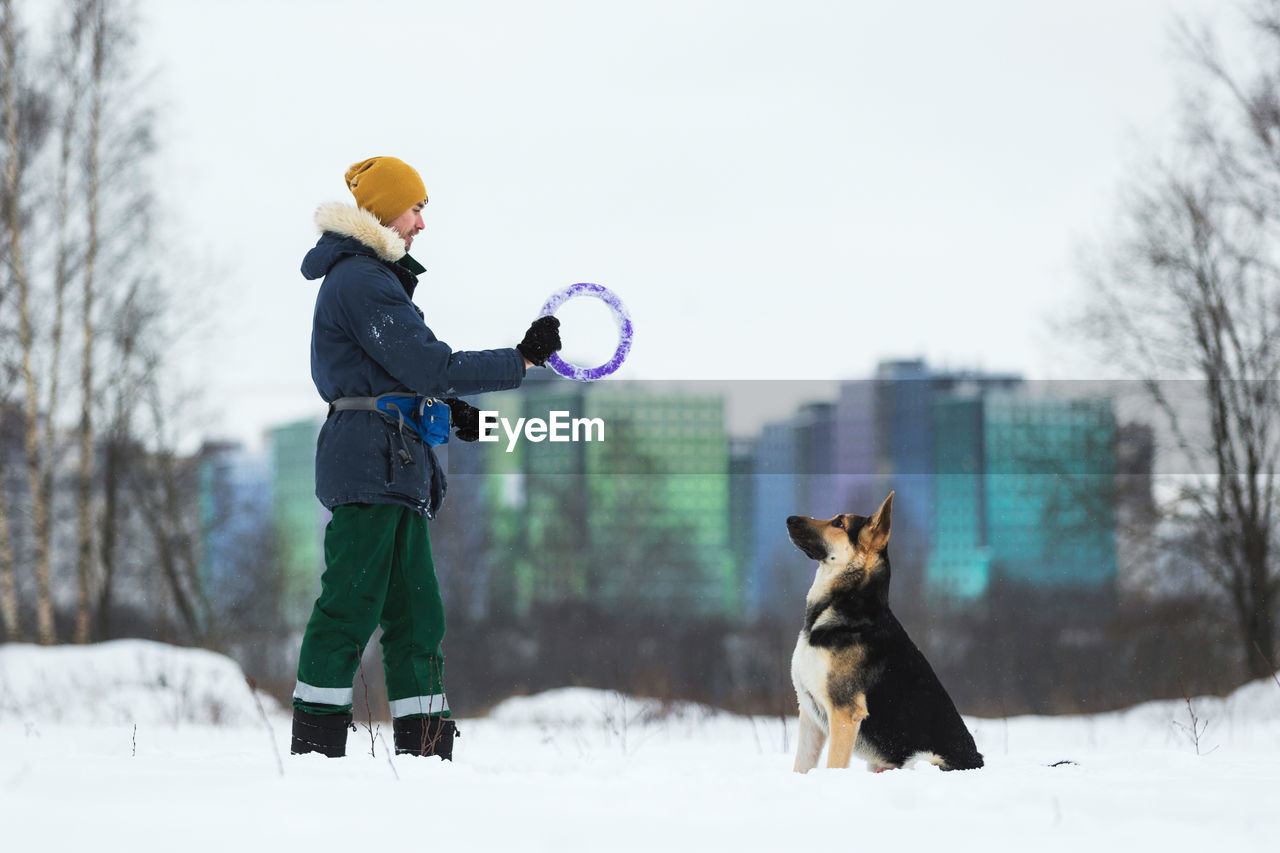 Man playing with dog in snow against sky