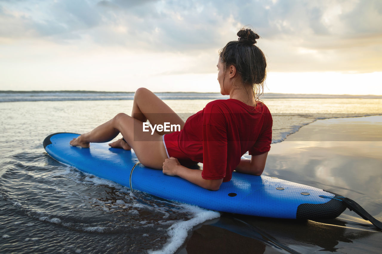 Woman sitting on surfboard on the beach after her surfing session