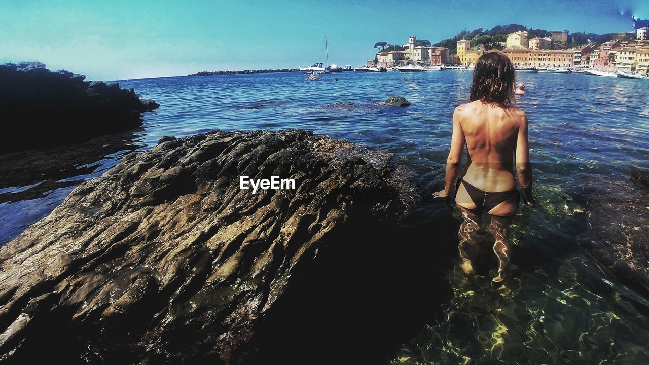 Rear view of semi-naked woman in sea against sky