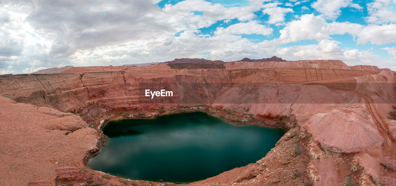 View of rock formations and lake against cloudy sky