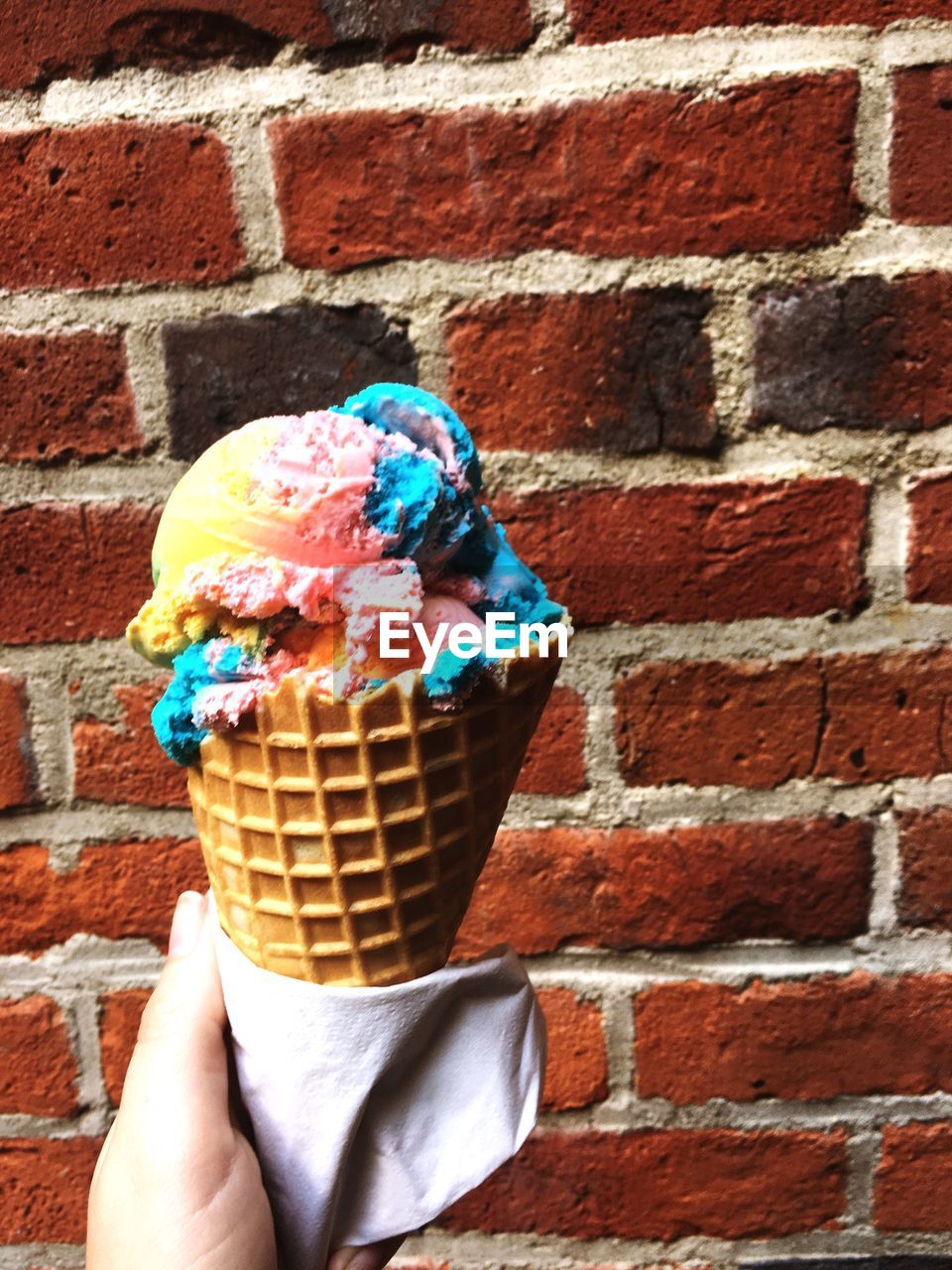 Close-up of hand holding ice cream cone against brick wall