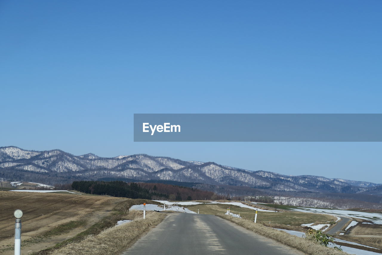 Road leading towards mountains against clear blue sky