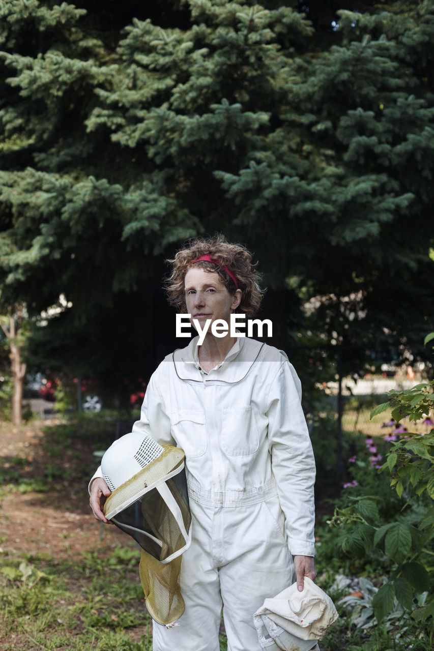 Portrait of confident senior beekeeper wearing protective suit standing on field