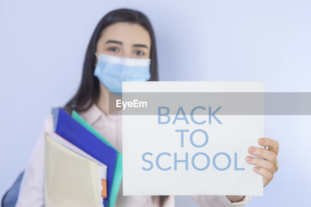 High school girl with mask on her showing back to school message. focus on her hand with paper.