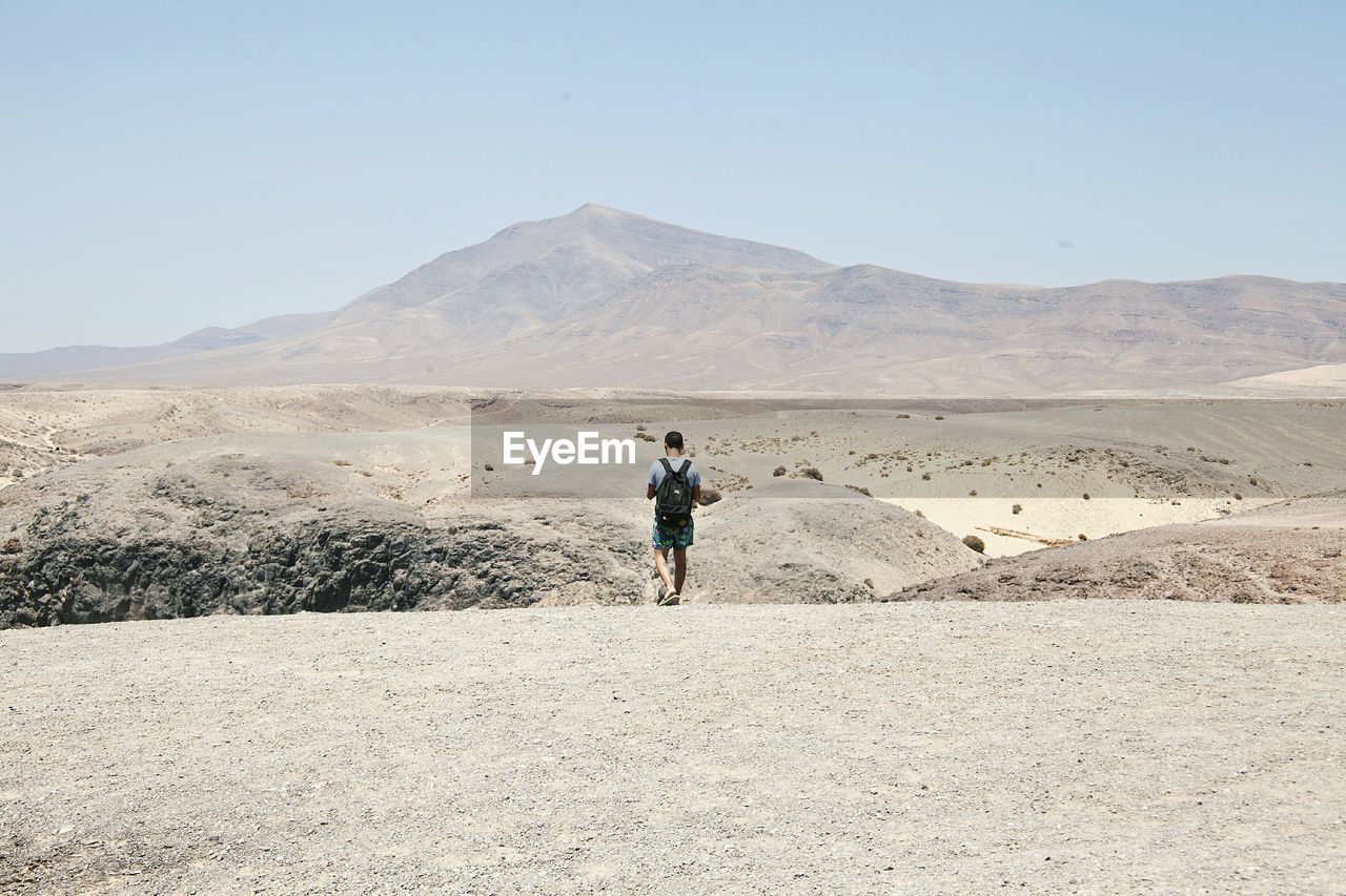 Rear view of hiker walking in desert against clear sky
