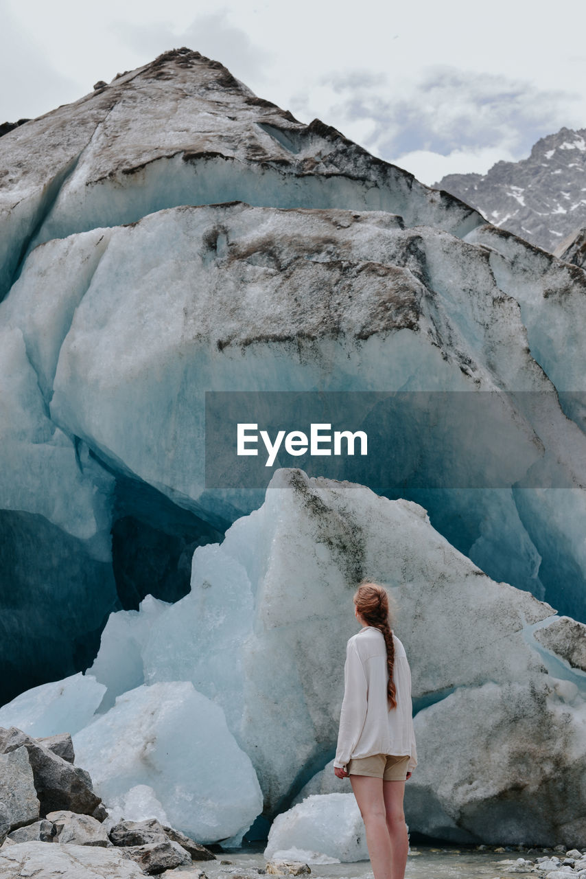 FULL LENGTH REAR VIEW OF WOMAN STANDING ON SNOW COVERED MOUNTAIN