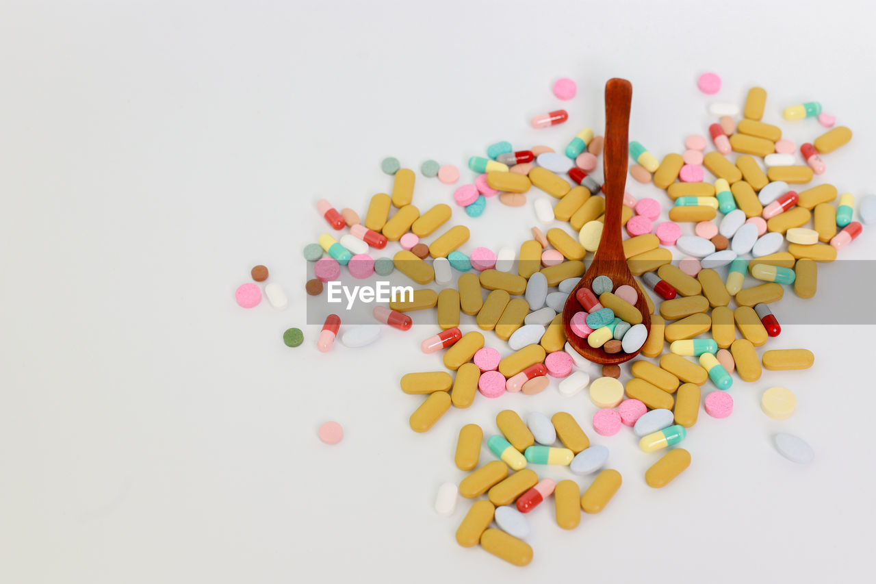 High angle view of multi colored pills with wooden spoon on white background