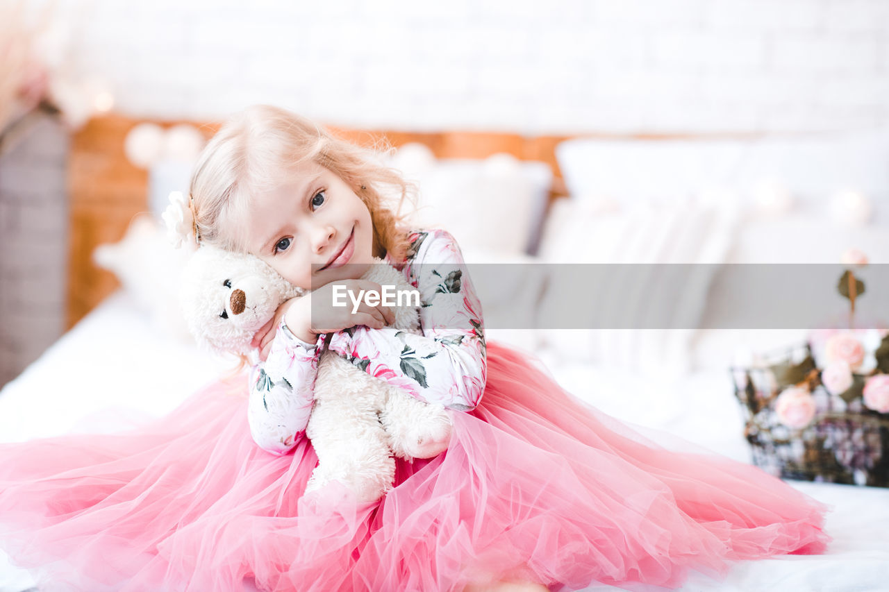 Girl embracing teddy bear sitting on bed