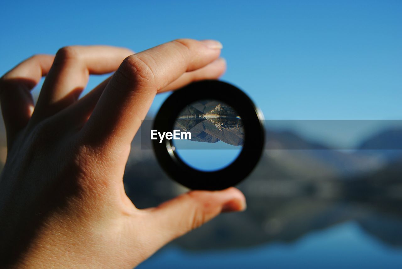 Cropped hand holding lens with upside down reflection of mountains