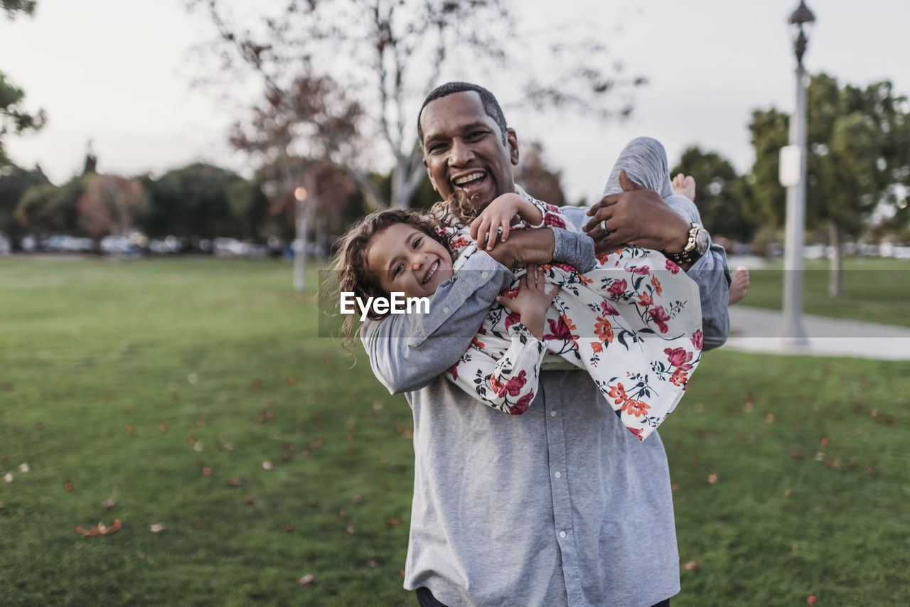 Happy father holding cute girl at park playground at dusk