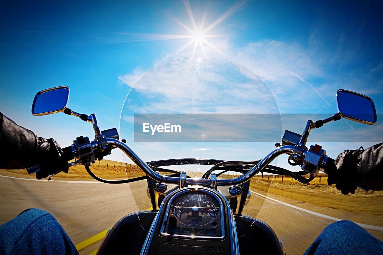 Motorbike speeding in front of long rural road against sun