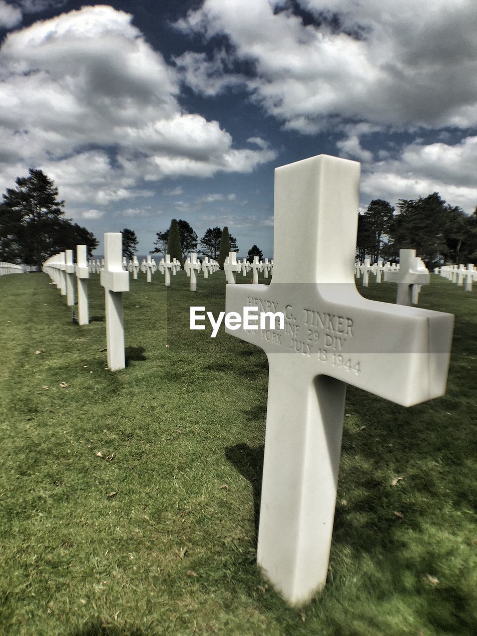 Cross on grassy field at military cemetery against cloudy sky