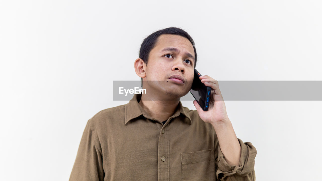 PORTRAIT OF YOUNG MAN LOOKING AWAY OVER WHITE BACKGROUND