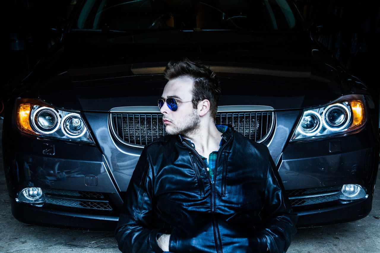 Front view of man sitting against car