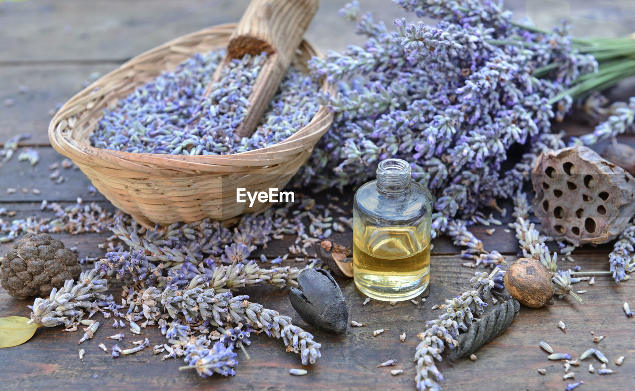 Lavender flowers petals in a little basket with essential oil bottle on a wooden table