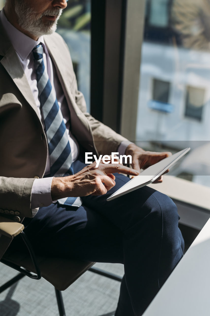 Businessman with tablet pc sitting on chair by window in office