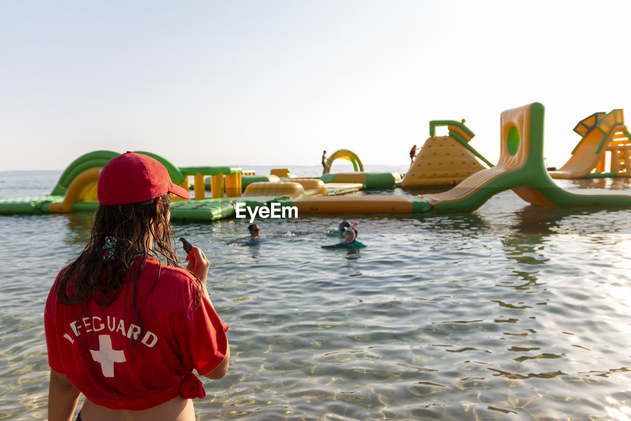 Lifeguard on rescue duty, standing on shore with whistle and looking to the aquapark. safety control
