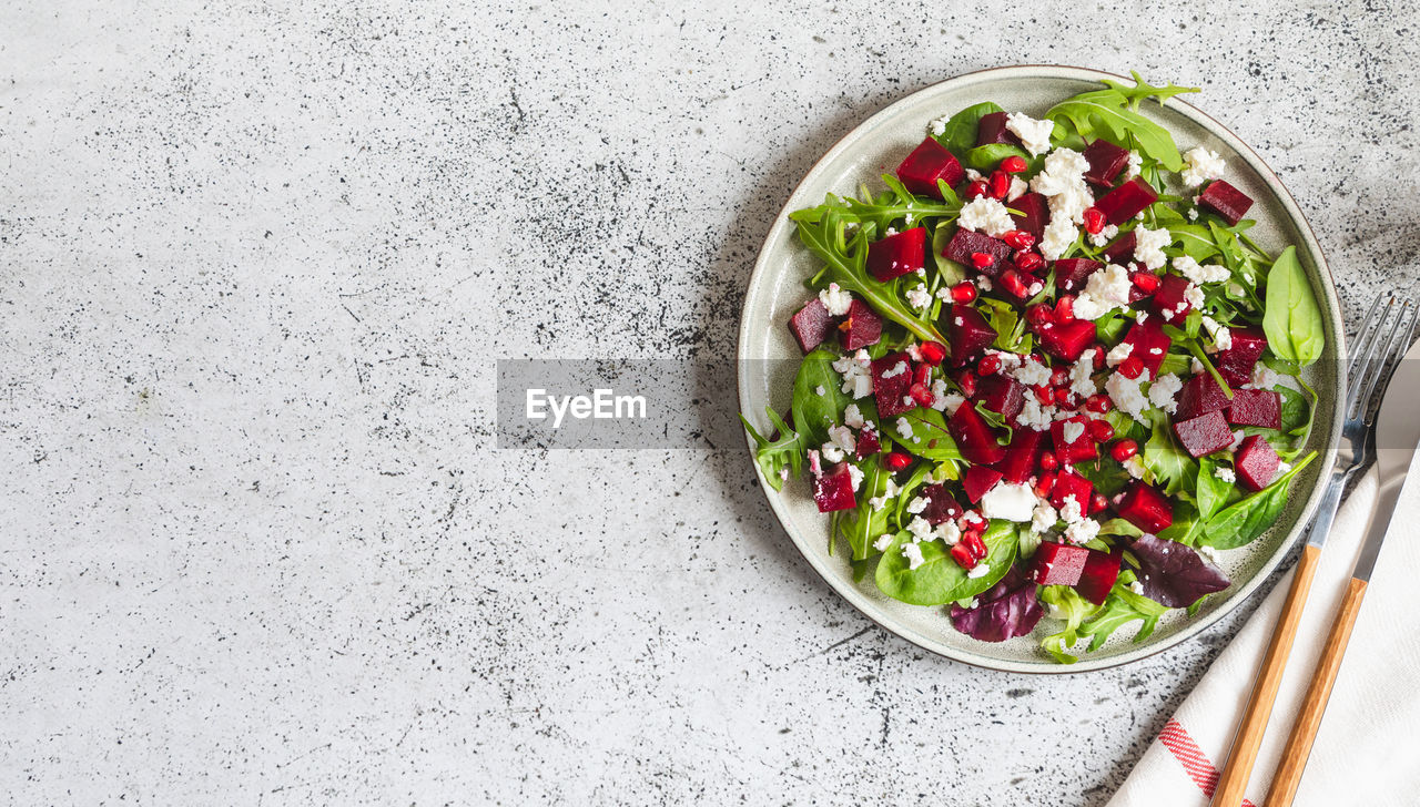 Arugula, beet and cheese salad with pomegranate and dressing on plate on grey stone kitchen table