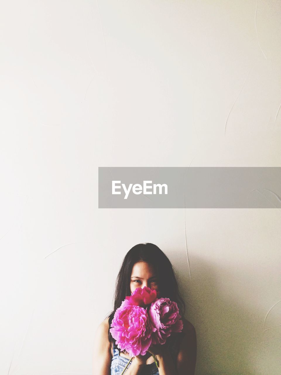 Portrait of woman holding pink flowers against white wall