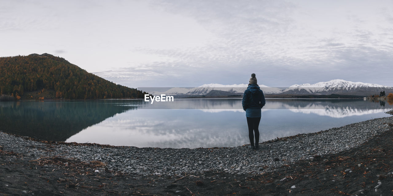 Young woman stands in front of lake tekapo and the southern alps