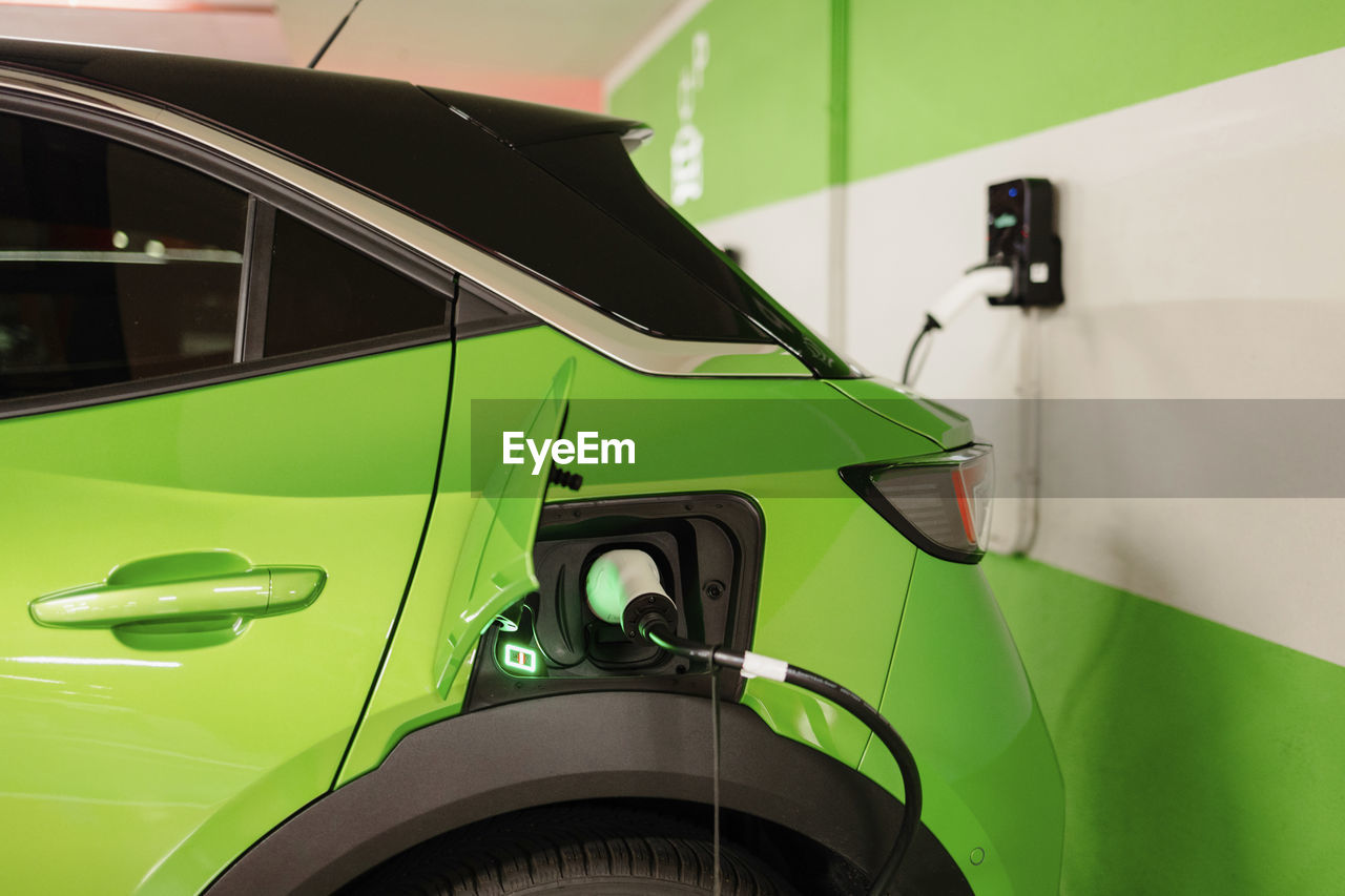 Green electric car being charged by wall at charging station