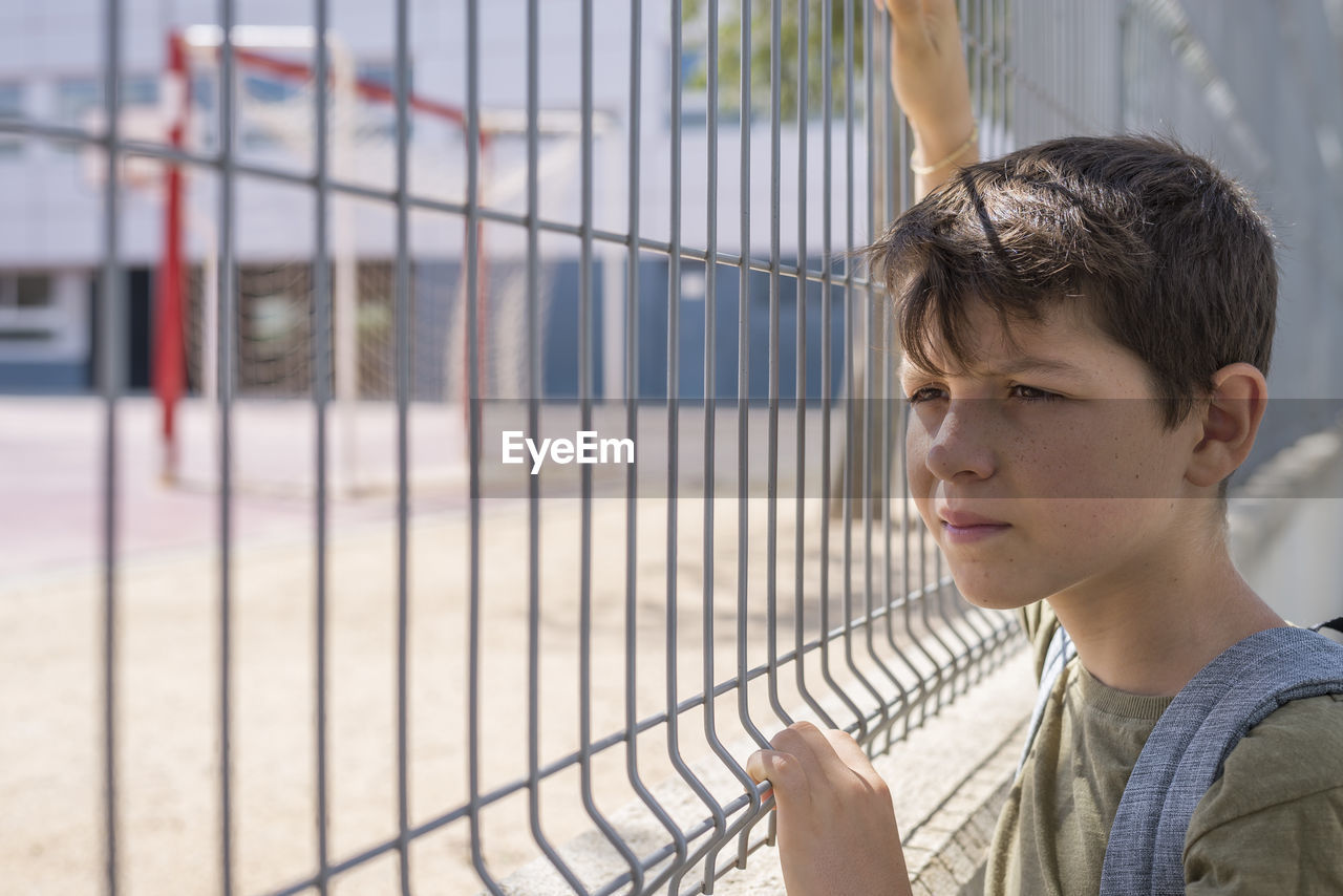 Boy standing by fence in schoolyard