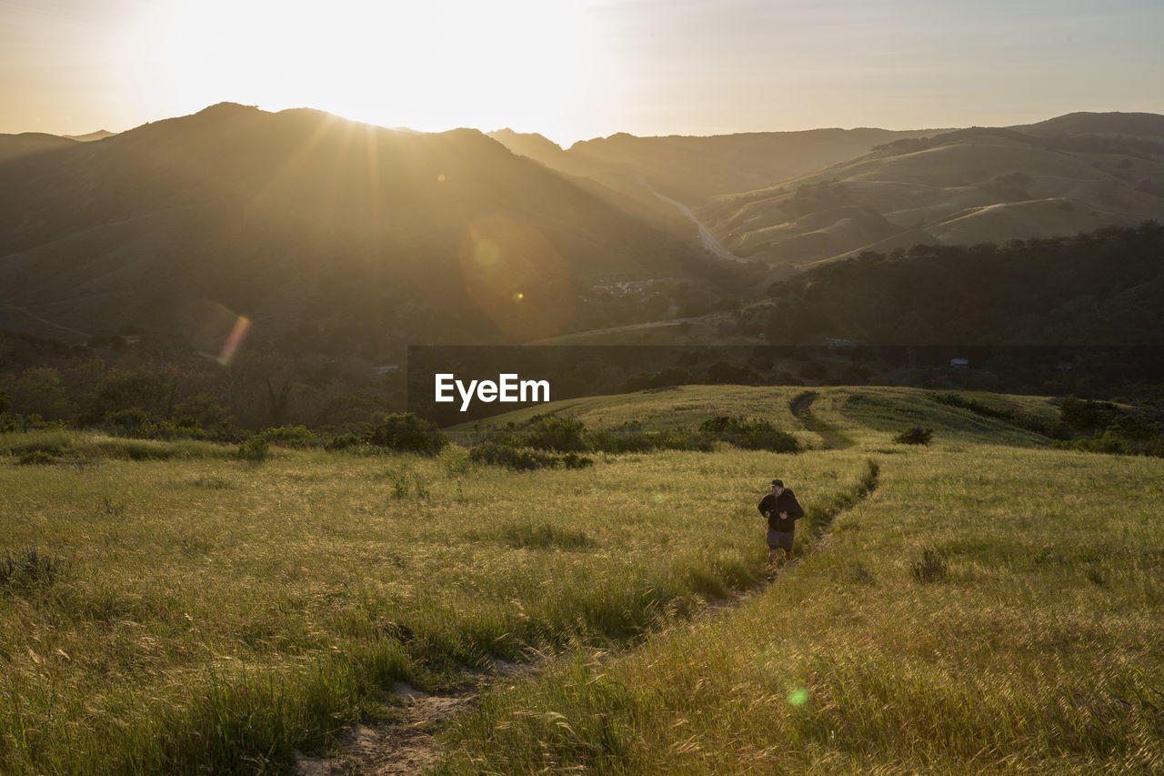 High angle view of man on trail amidst grassy field against mountains during sunset