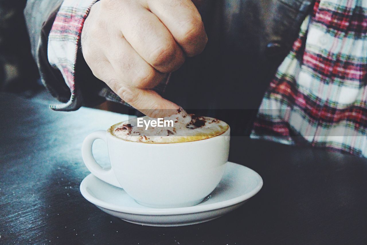 Midsection of man with finger in coffee on table at home