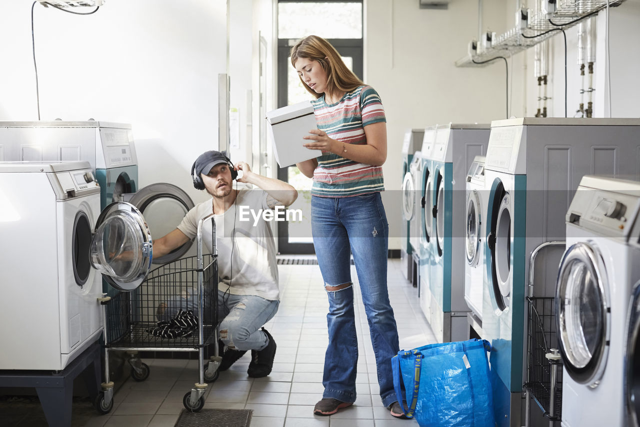 Confused university student showing detergent pack to male friend at laundromat