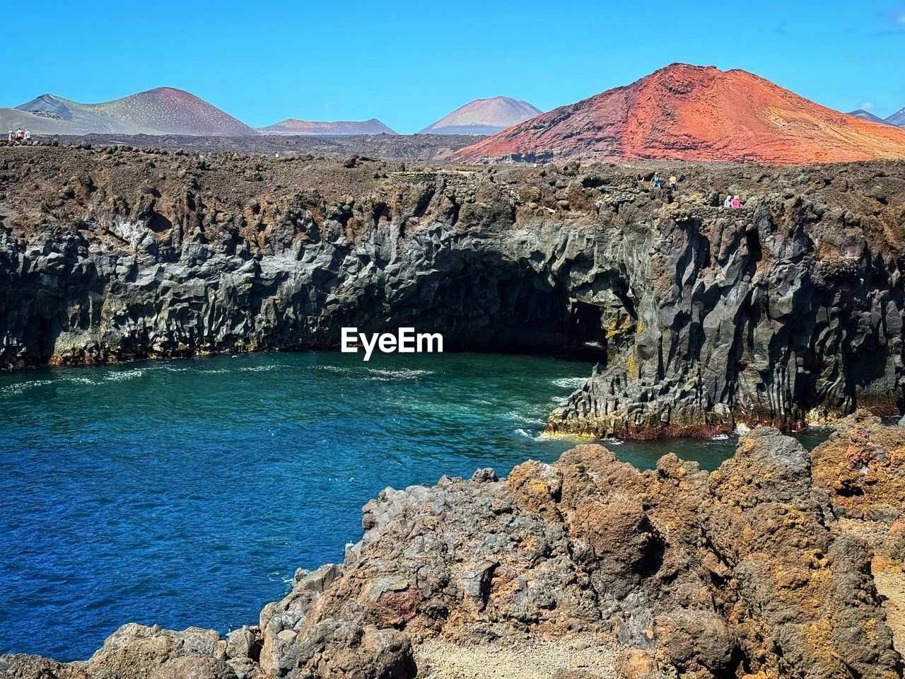 water, mountain, scenics - nature, beauty in nature, sea, landscape, rock, nature, environment, coast, land, sky, geology, blue, travel destinations, non-urban scene, cliff, wilderness, no people, volcano, tranquility, travel, clear sky, tranquil scene, terrain, day, shore, rock formation, mountain range, outdoors, bay, sunny, tourism, idyllic, extreme terrain, wadi, physical geography, sunlight