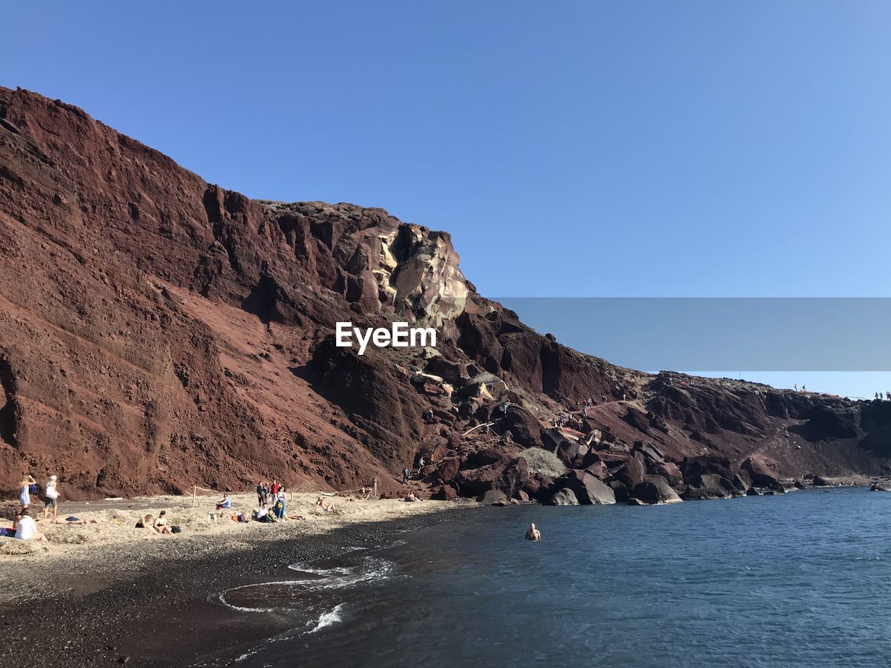 People on rocks by sea against clear sky