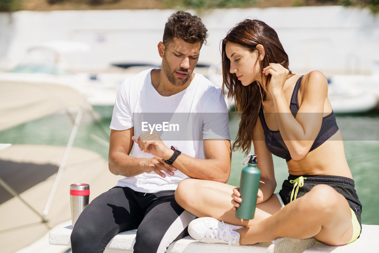 Couple checking time while sitting at harbor