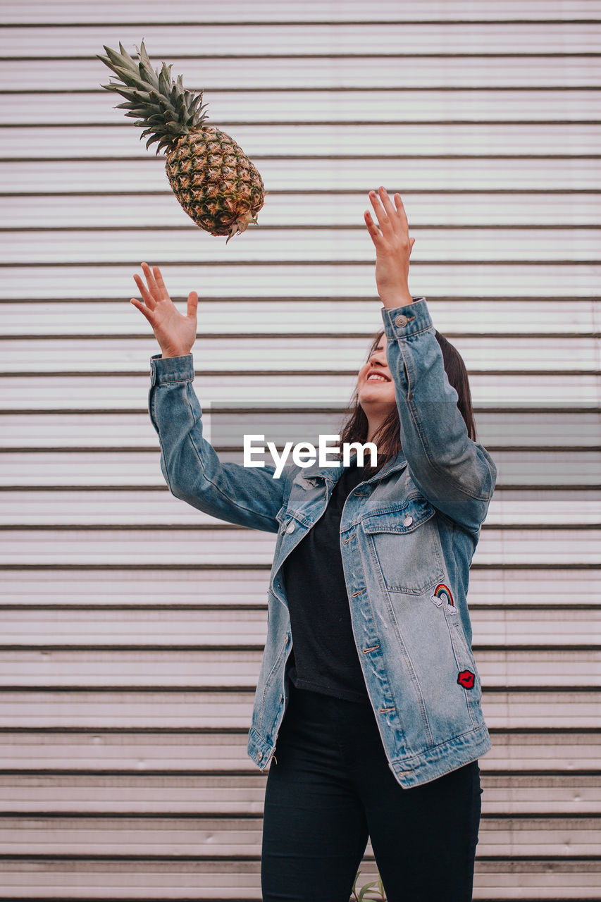 Woman playing with pineapple while standing against wall